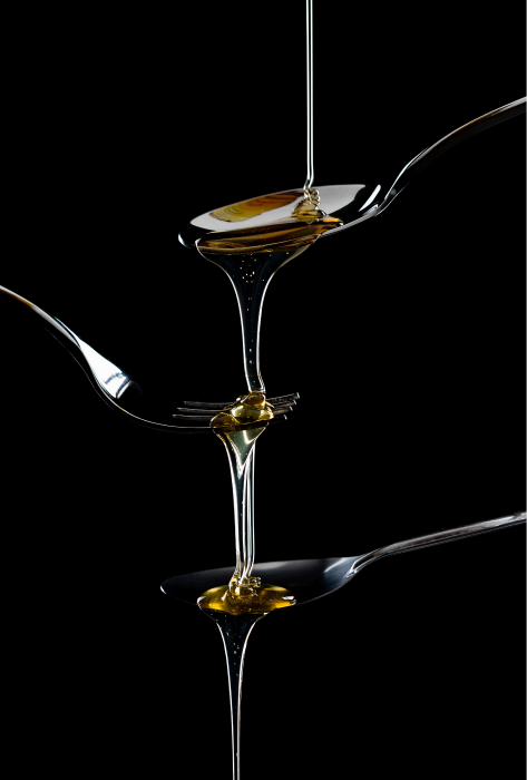 Close-up of spoons with honey slowly dripping off, highlighting the rich, amber color and smooth consistency.