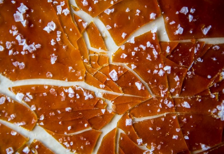 cracked caramel top, likely on a dessert such as crème brûlée. The caramel is golden brown with a glossy finish and is sprinkled with sea salt flakes.