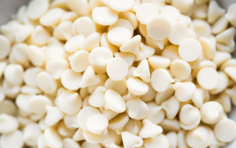 Close-up of a pile of white chocolate chips. The chips are small, round, and have a smooth texture,